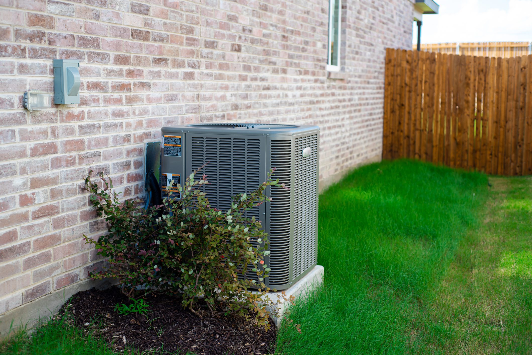 Outdoor HVAC condenser next to brick house