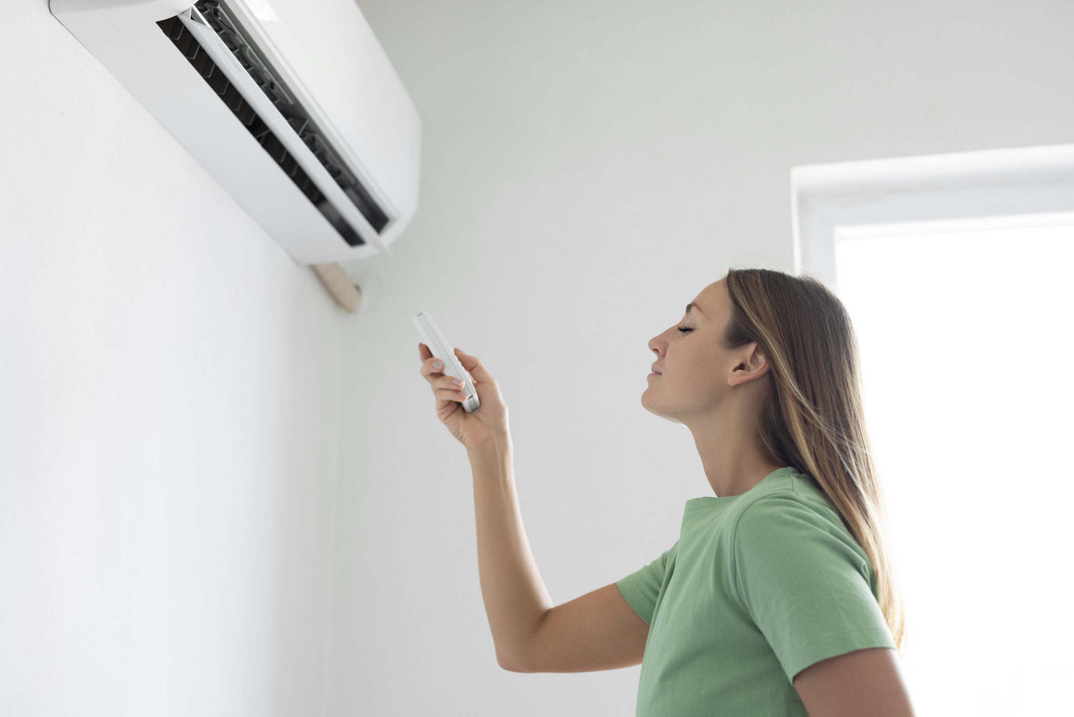Woman using remote for wall-mounted air conditioner