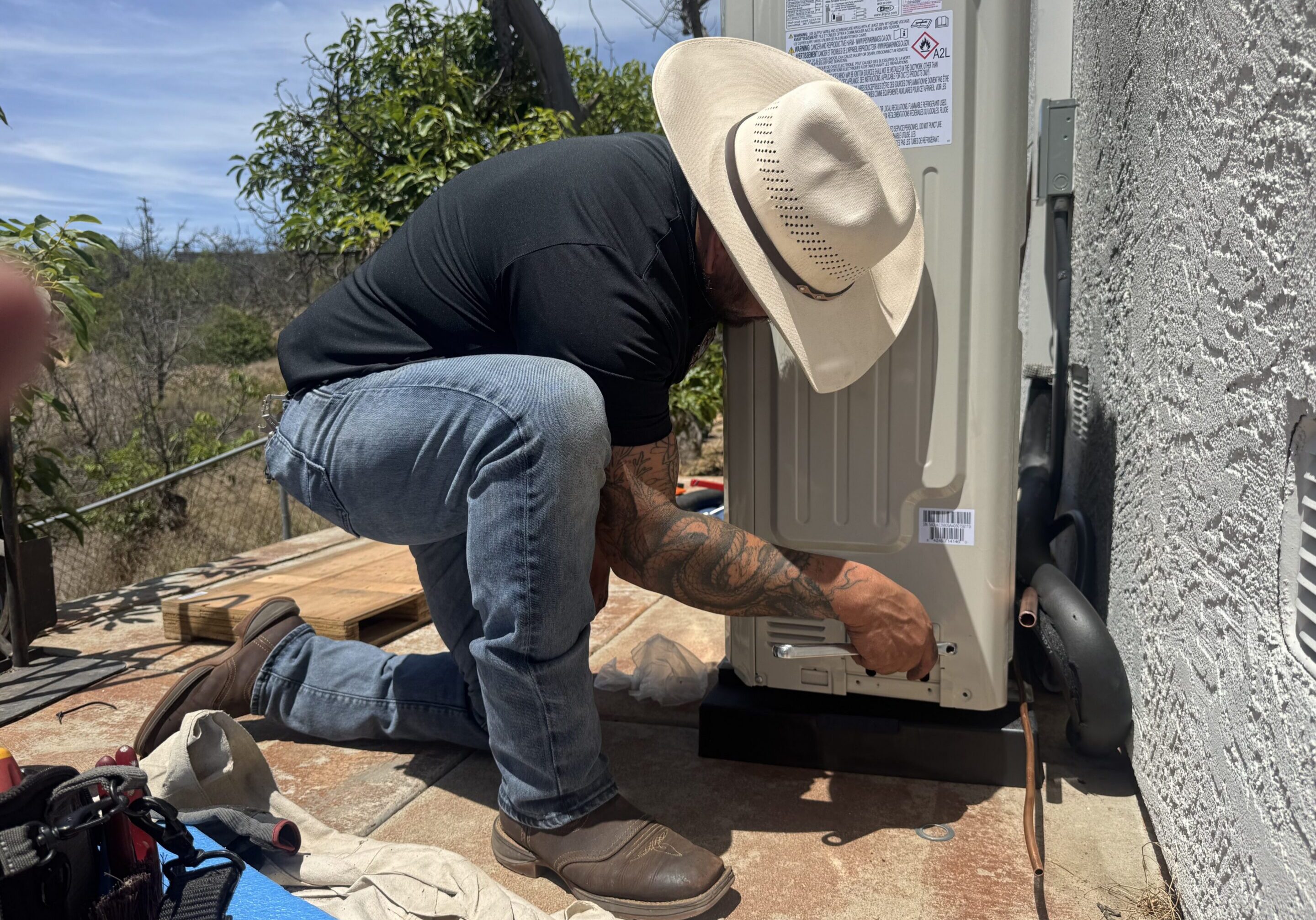 Worker in cowboy hat installs outdoor AC unit