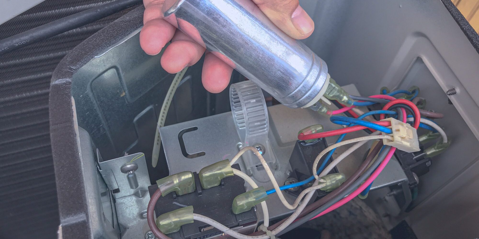 Hand holding air conditioner capacitor near wiring