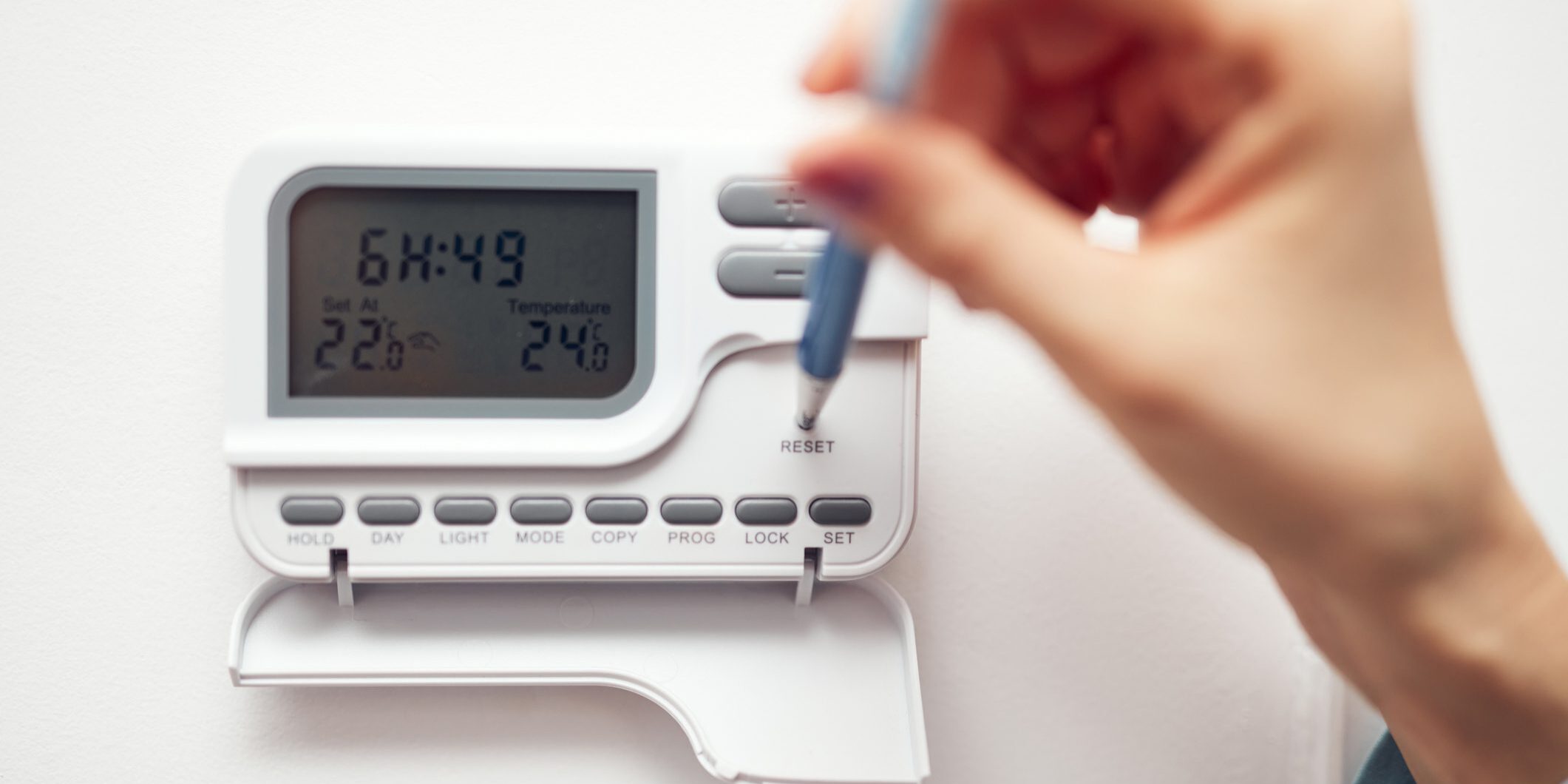 Hand programming digital thermostat on wall