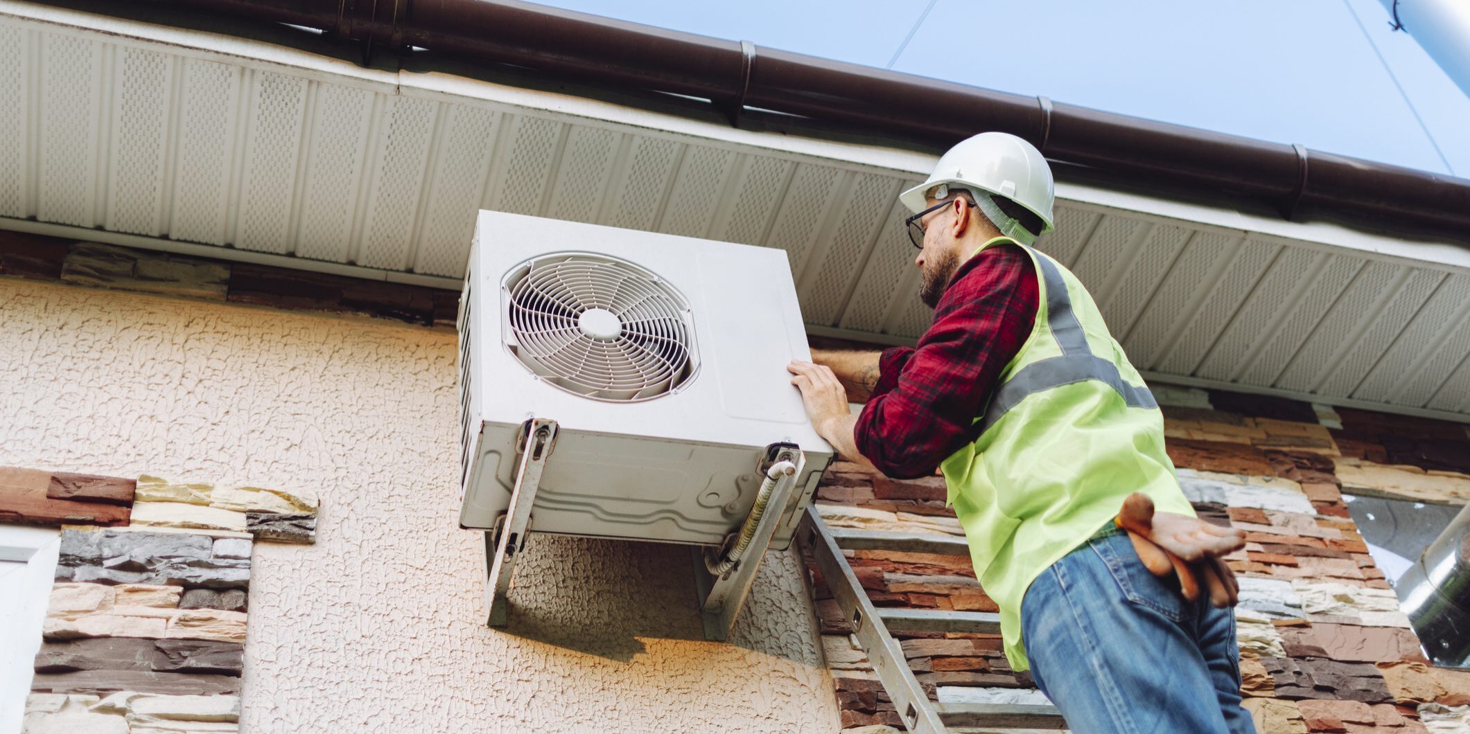 HVAC technician installing outdoor air conditioner on ladder