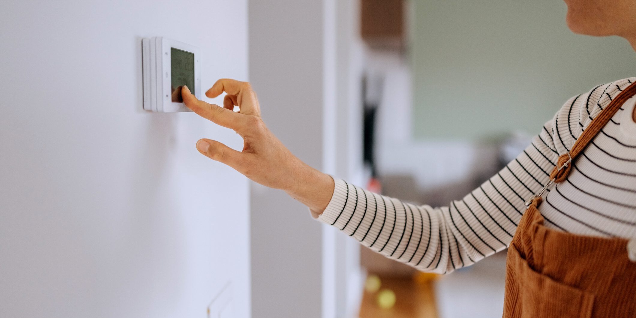 Person adjusting thermostat on wall